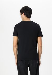 Camiseta negra de manga corta con cuello redondo, hecha de algodón suave. La parte trasera presenta una textura lisa y un diseño minimalista.