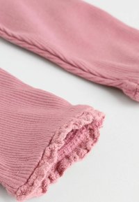Roze rebrasti materijal, mekan na dodir, s volanim rubom. Glatki, uski oblik s dosljednim uzorkom, naglašava toplinu materijala.