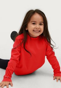 Roter Sweatshirt mit hohem Kragen und langen Ärmeln. Glattes Material, lockere Passform. Kind sitzt auf dem Boden, trägt schwarze Hose und Schuhe.
