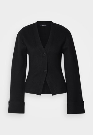 Svart cardigan med djup V-hals, två knappar och vida ärmar. Tyget verkar slätt, med en figurnära design och skräddarsydda manschetter.