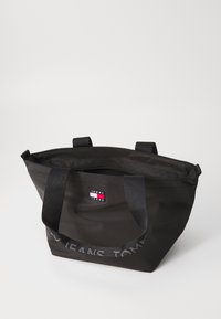 Schwarze Tragetasche mit doppelten schwarzen Griffen, aus Nylon gefertigt. Verfügt über eine Reißverschlusstasche und ein Logo-Patch mit roten, weißen und blauen Details.