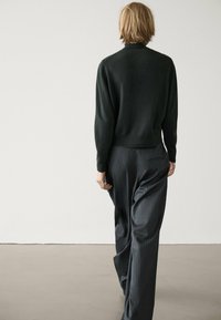 Pull en maille noire avec un col montant, associé à un pantalon large à fines rayures foncées. La tenue présente une coupe décontractée et texturée.
