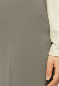 Grauer Stoff, strukturiert und glatt, fällt über eine Hand. Ein hellfarbener Ärmel ist teilweise auf der rechten Seite sichtbar und kontrastiert mit dem Stoff.