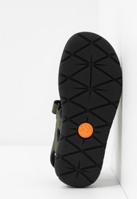 Suola esterna in gomma nera con motivo battistrada testurizzato e logo circolare arancione. Tomaia in tessuto verde scuro con cinturino regolabile.