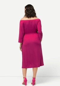 Fuksia off-the-shoulder mekko, jossa on kolmennes-hihat, vyötärövyö, polven keskivaiheelle ulottuva pituus ja teksturoitu kangas. Yhdistettyinä yhteensopiviin vaaleanpunaisiin korkokenkiin.