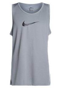 Camiseta deportiva sin mangas gris hecha de tela ligera y que absorbe la humedad. Presenta un escote redondeado y un logo negro de Nike impreso en el frente.
