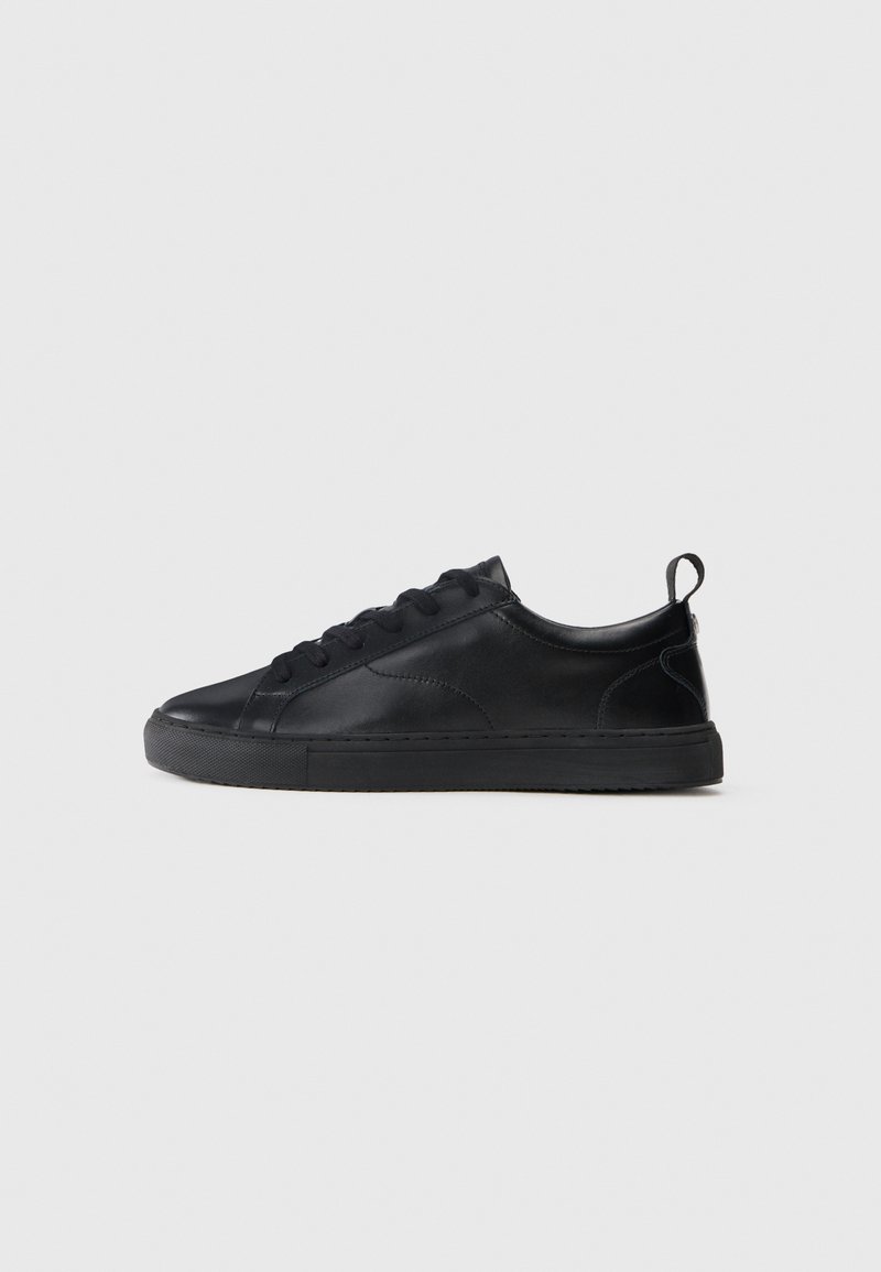 Black leather sneaker with a smooth texture, lace-up design, flat rubber sole, and a small back loop for easy wear. Subtle stitching accents.