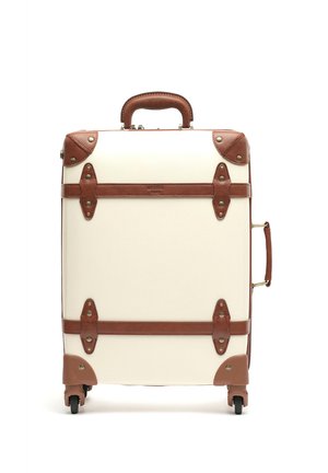 Hard-sided suitcase in cream with brown leather accents. Features a top handle, front straps, metal hardware, and four wheels.