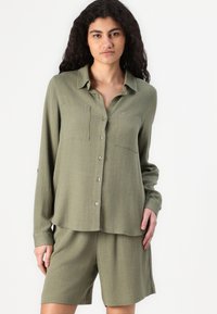 Olijfgroene button-up shirt met twee voorzakken, zachte stof, lange mouwen en bijpassende shorts in een relaxte pasvorm.