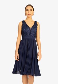Marineblaues Kleid mit einem gefalteten Rock und besticktem Spitzentop. Verfügt über einen tiefen V-Ausschnitt und breite Träger. Weicher, fließender Stoff.