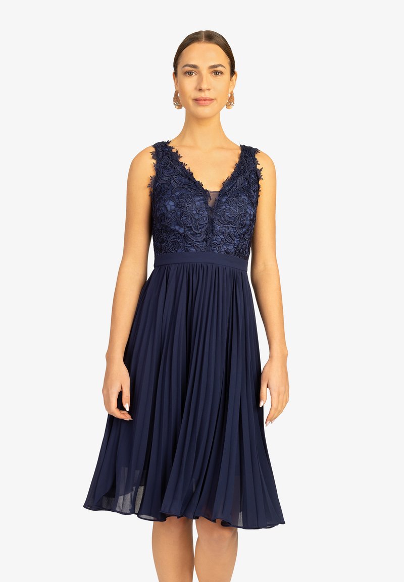 Marineblaues Kleid mit einem gefalteten Rock und besticktem Spitzentop. Verfügt über einen tiefen V-Ausschnitt und breite Träger. Weicher, fließender Stoff.