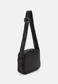 Black leather crossbody bag with a rectangular shape, textured surface, and a branded strap featuring the name "Valentino."