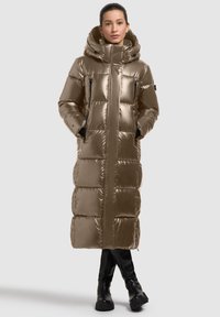 Long, shiny beige puffer coat with a hood, featuring a quilted design, side pockets, and a straight silhouette. Worn over black knee-high boots.