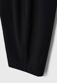 Partie inférieure d'un pantalon noir sur mesure avec une jambe droite et fuselée et une couture visible au centre.