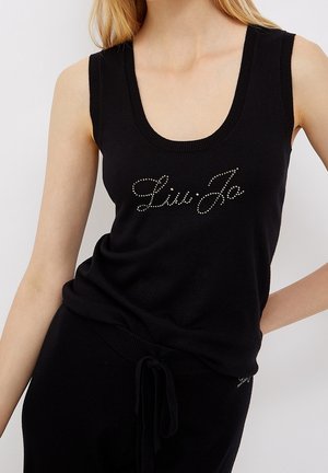 Kobieta ubrana w czarny, bezrękawnikowy dzianinowy top z okrągłym dekoltem i napisem "Liu Jo" z kryształków na piersi.