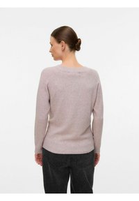 Ljust rosa ulltröja med ribbad halsringning och långa ärmar, med en slät textur och en figursydd silhuett, kombinerad med mörka jeans.