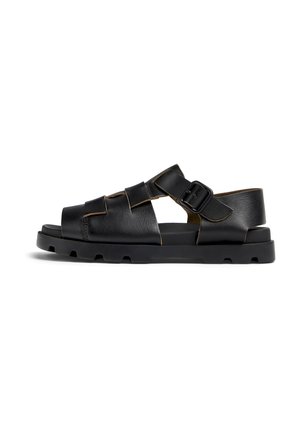 Des sandales en cuir noir présentent un design à lanières avec une boucle sur le côté, un bout rond et une semelle noire épaisse avec une texture antidérapante.