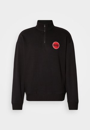 Musta neljandiku lukuga sviiter ribidega varrukates ja hemil. Omab punast ringikujulist logo, millel on tekst "HUGO". Valmistatud siledast ja kergekaalulisest kangast.