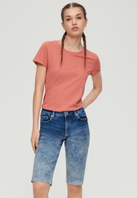 Korte mouwen, koraalkleurig T-shirt gecombineerd met denim shorts met een lichte naar donkere ombre-effect, vijf zakken en een rafelige zoom.