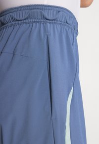 Shorts de sport bleus avec taille élastique, dotés de poches latérales et d'un détail en mesh bleu clair sur la jambe pour la respirabilité.