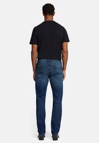 Granatowe dżinsy o prostym kroju, z dwoma tylnymi kieszeniami i średnim stanem, w zestawieniu z czarną koszulką.