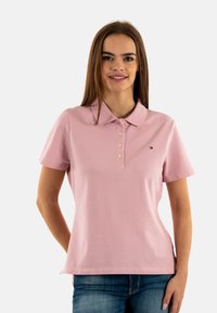 Polo rosa con maniche corte, colletto e patta con tre bottoni. Presenta un piccolo logo sul petto a sinistra. Materiale in cotone.