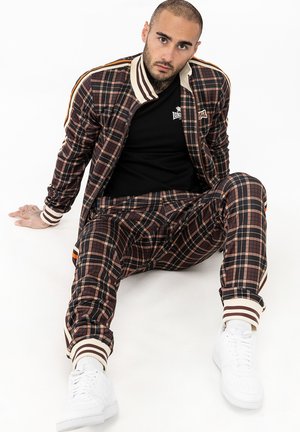 Ruda, smėlio ir oranžinės spalvų derinio plaid treningas, su juostuotais rankogaliais ir užtrauktuku užsegamu švarku. Balti sportbačiai papildo įvaizdį.