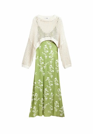Maglione corto lavorato a maglia color crema abbinato a un lungo vestito verde con motivi floreali bianchi. Il vestito ha un corpetto aderente e una gonna svasata.
