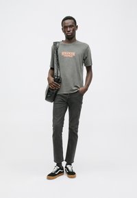 Gray t-shirt with "STRANGER THINGS" logo, black shoulder bag, gray pants, and black sneakers with white accents and gum sole.
