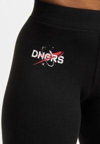 Sorte leggings laget av et elastisk materiale har et hvitt og rødt grafisk design med teksten "DNGRS" og rom-tematiske detaljer.