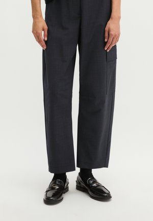 Person wearing black wide-leg pants with side cargo pocket and black leather loafers with black socks on a white background.