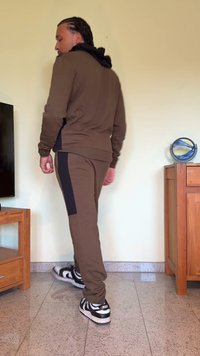 Brown tracksuit with a black hooded jacket, featuring side panels on the pants. Black and white sneakers complete the outfit.