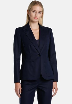 Blazer sartoriale blu navy in tessuto liscio, con un bottone singolo, rever a punta e due tasche a toppa frontali. Design aderente, maniche lunghe.