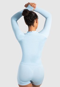 Lyst blå atletisk bodysuit med lange ærmer, ribbet tekstur, høj krave og korte ben. Har tommelfingerhuller ved ærmeenderne.