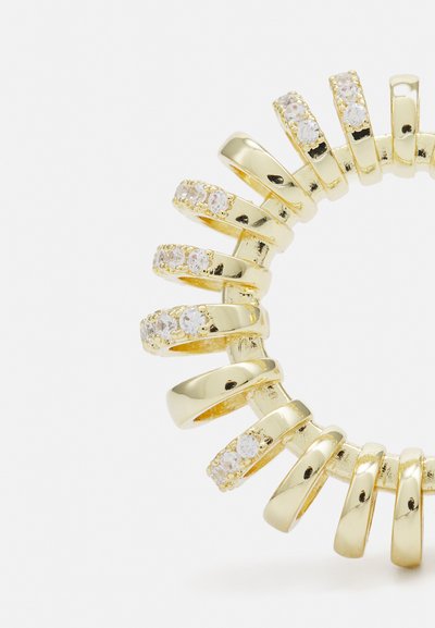 Gold-colored circular ring with multiple overlapping bands, featuring clear crystal accents on some bands, smooth and polished texture.