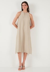 Beige sleeveless midi dress with a gathered neckline, lightweight texture, and a straight silhouette, paired with multicolored heeled sandals.