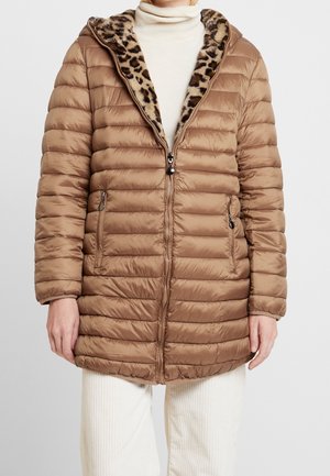 Gouden gewatteerde pufferjas met binnenvoering van luipaardprint, ritssluiting en ritssluitingen aan de zakken, gedragen over een witte coltrui en crèmekleurige broek.