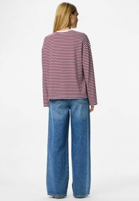Dlouhá rukávová košile pruhovaná v maroon a růžové barvě, spárovaná s širokými modrými džíny s volným střihem a texturovanou tkaninou.