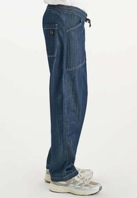 Donkerblauwe denim broek met een relaxte pasvorm, voorzien van een koord taille en zijzakken. Zachte textuur met contrasterende witte stiksels.
