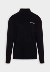 Musta pitkähihainen korkea kauluspaita, jossa on rintatasku ja vasemmalla puolella valkoinen "HILFIGER"-teksti.