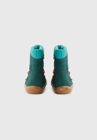Bottines en daim vert avec un col texturé turquoise, des lacets orange et une semelle en caoutchouc marron. Vue arrière montrant les détails de design et de matériau.
