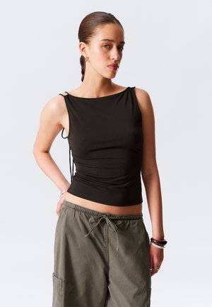 Top noir sans manches avec liens sur les côtés, design ajusté, texture douce, associé à un pantalon cargo vert olive ample avec poches.