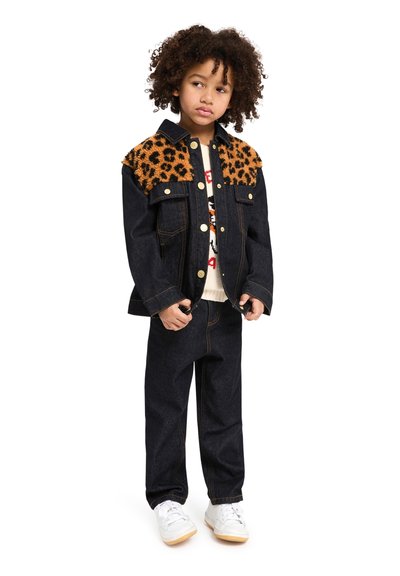 Veste en denim avec épaules en imprimé léopard, tissu bleu foncé, fermeture à boutons, deux poches poitrine, portée avec un pantalon en denim foncé et des baskets blanches.