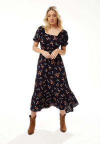 Black floral dress with puff sleeves, square neckline, ruffled hem, and a textured fabric. Worn with brown cowboy boots.