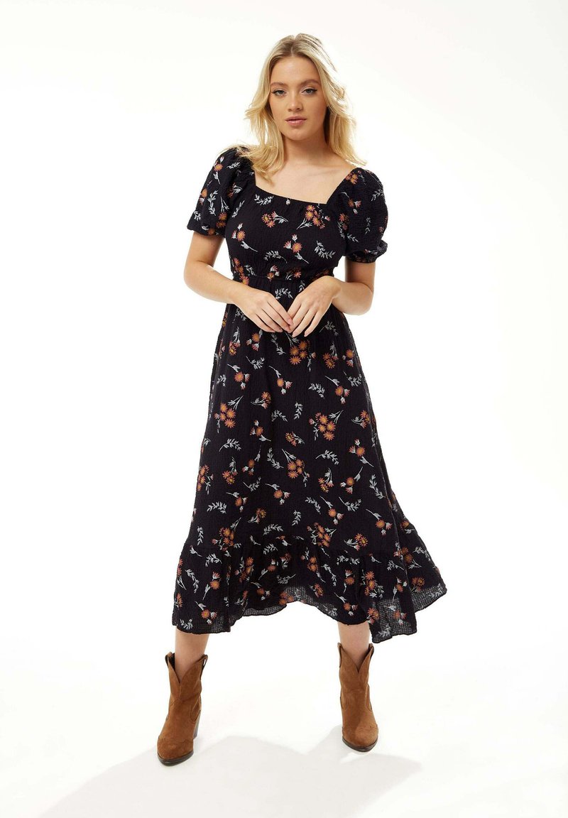 Black floral dress with puff sleeves, square neckline, ruffled hem, and a textured fabric. Worn with brown cowboy boots.
