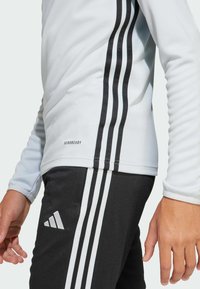 Lichtblauw sportshirt met lange mouwen en zwart drie-strepen ontwerp op de mouwen, gecombineerd met zwarte broek met een witte drie-strepen detail en logo.
