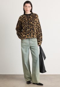 Svetr s leopardím vzorem v hnědé a černé barvě, oversize střih, kombinovaný se světlomodrými širokými džínami a černou kabelkou. Hladká textura, ležérní design.