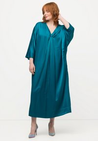 Tyrkysové saténové dlouhé šaty s výstřihem do V a širokými rukávy, s volným, splývavým tvarem a jemným drapováním. Hedvábná textura podtrhuje eleganci.