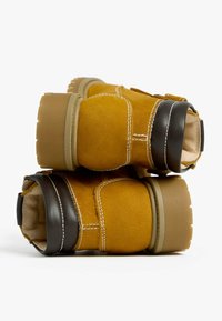 Stivaletti alla caviglia gialli in suede con una superficie texturizzata, accenti marroni a contrasto e una suola spessa con scanalature profonde. Dettagli cuciti presenti.