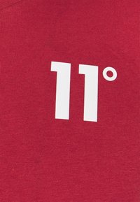 Tessuto di cotone rosso con una grande grafica bianca che mostra i numeri "11" e un simbolo di grado, centrata sulla superficie.